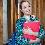 Smiling student holding book and wearing headphones, ready for study.